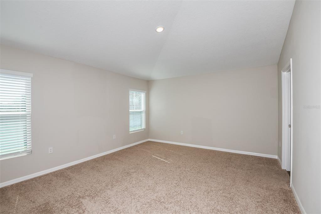An empty bedroom features beige walls, tan carpeting, two windows with blinds, and a doorway — 5393 SAN PIETRO DRIVE, WINTER HAVEN, FL