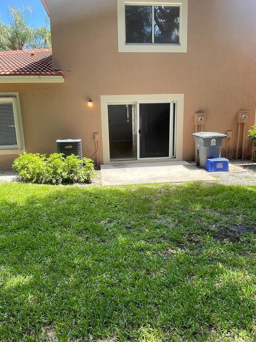 The exterior of a tan house features a sliding glass door, patio, and lawn — 9766 Kamena Circle, Boynton Beach FL 33436, BOYNTON BEACH, FL