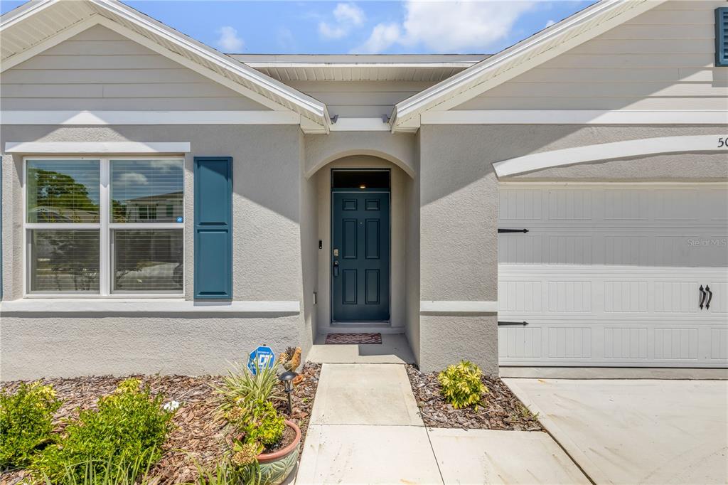 The exterior of a single-story house features a blue front door, garage, and landscaping — 507 CORONADO COVE ROAD, NEW SMYRNA BEACH, FL