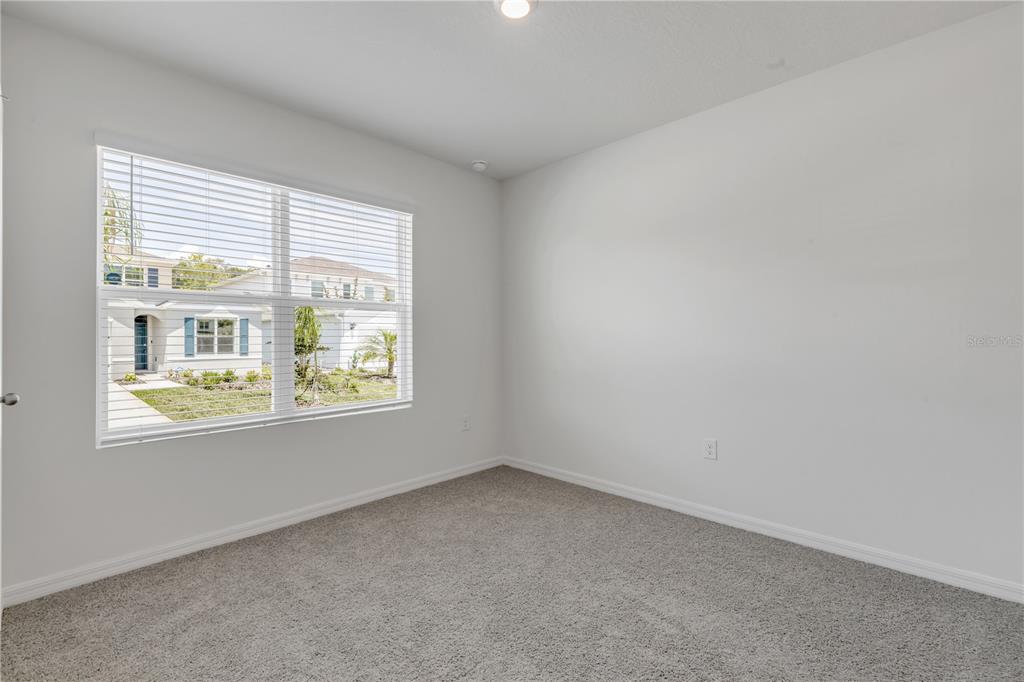 An empty room features gray carpet, white walls, and a window overlooking a suburban street — 507 CORONADO COVE ROAD, NEW SMYRNA BEACH, FL