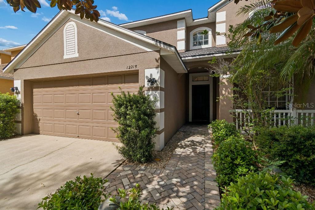 The exterior of a two-story house features a tan stucco facade, a garage, and landscaping — 12215 ADVENTURE DRIVE, RIVERVIEW, FL