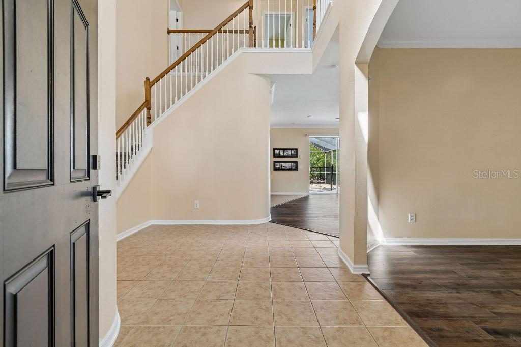 An entryway with tile flooring, a staircase with white railings, and wood-look flooring beyond — 12215 ADVENTURE DRIVE, RIVERVIEW, FL
