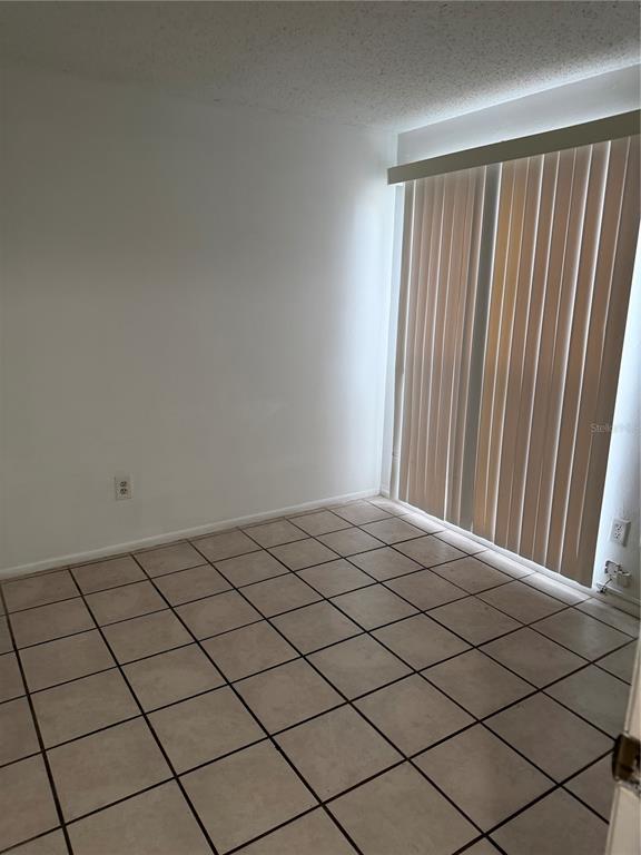 An empty room with beige tile flooring and vertical blinds covering a sliding glass door — 8237 RAVENCROFT DRIVE, TAMPA, FL