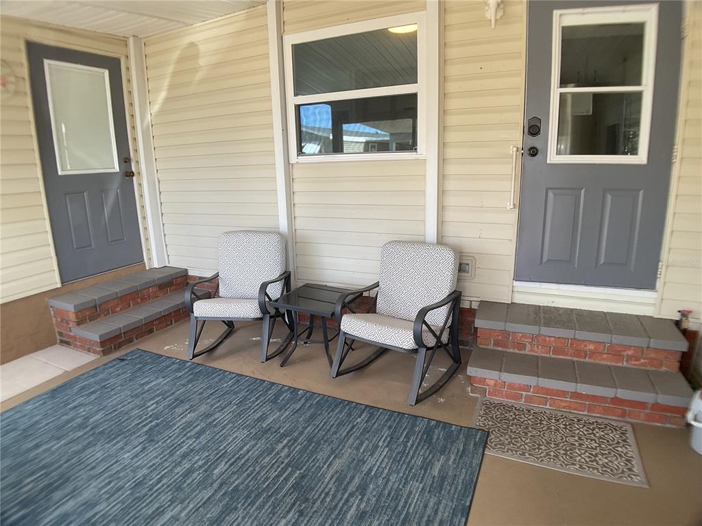A covered porch features two rocking chairs, a small table, and two gray exterior doors — 2100 KINGS HIGHWAY UNIT 577, PUNTA GORDA, FL