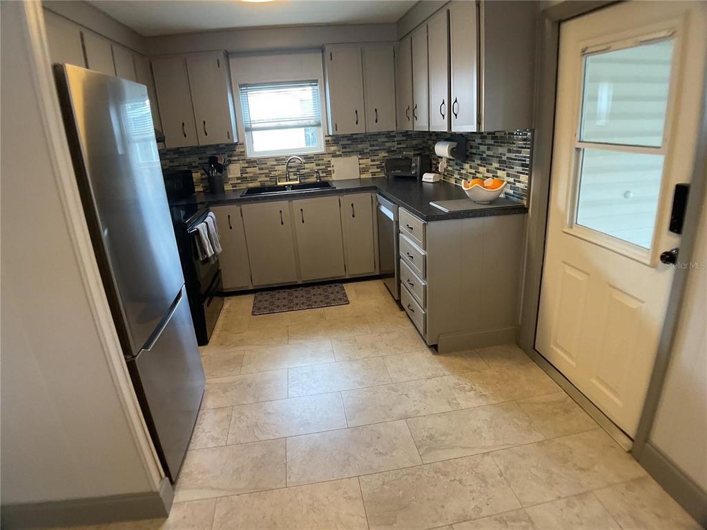 A kitchen features grey cabinets, stainless steel appliances, a tiled backsplash, and light-colored floor tiles — 2100 KINGS HIGHWAY UNIT 577, PUNTA GORDA, FL