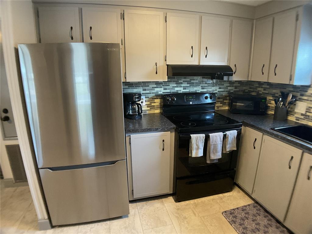 A kitchen features stainless steel appliances, light gray cabinets, and a mosaic tile backsplash — 2100 KINGS HIGHWAY UNIT 577, PUNTA GORDA, FL
