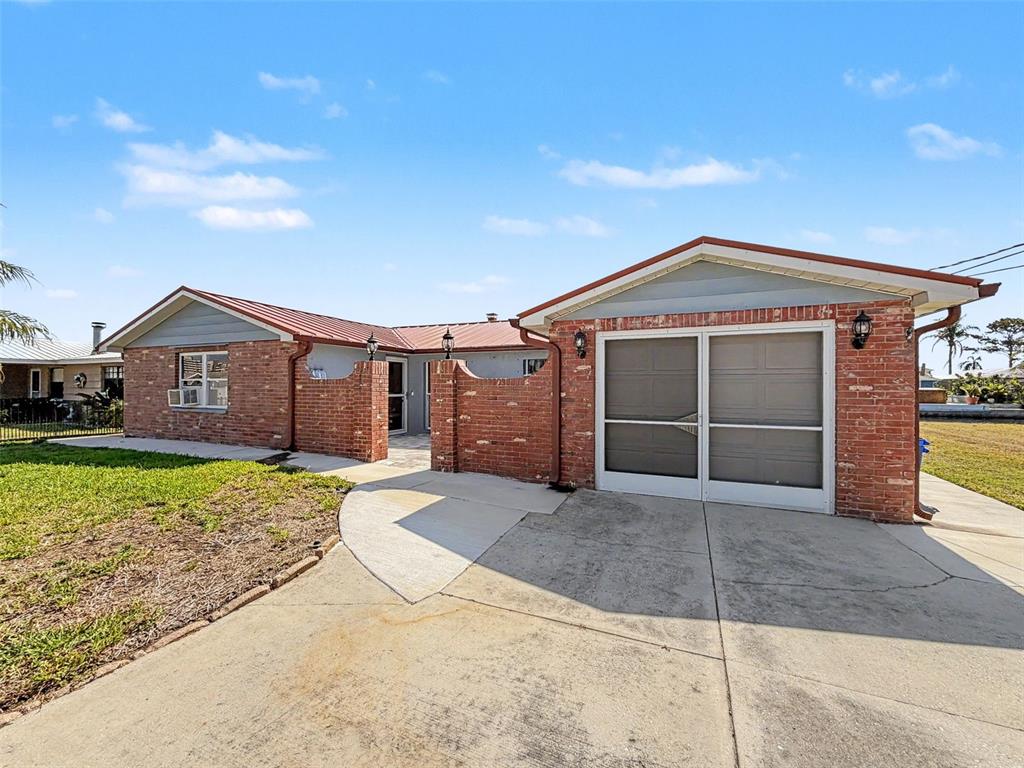 A single-story brick house features a metal roof, a driveway, and a screened-in garage — 13520 ALLYN DRIVE, HUDSON, FL