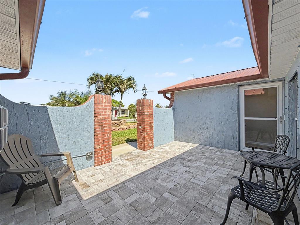 A paved patio features a brick-pillared wall, outdoor seating, and a view of the yard — 13520 ALLYN DRIVE, HUDSON, FL