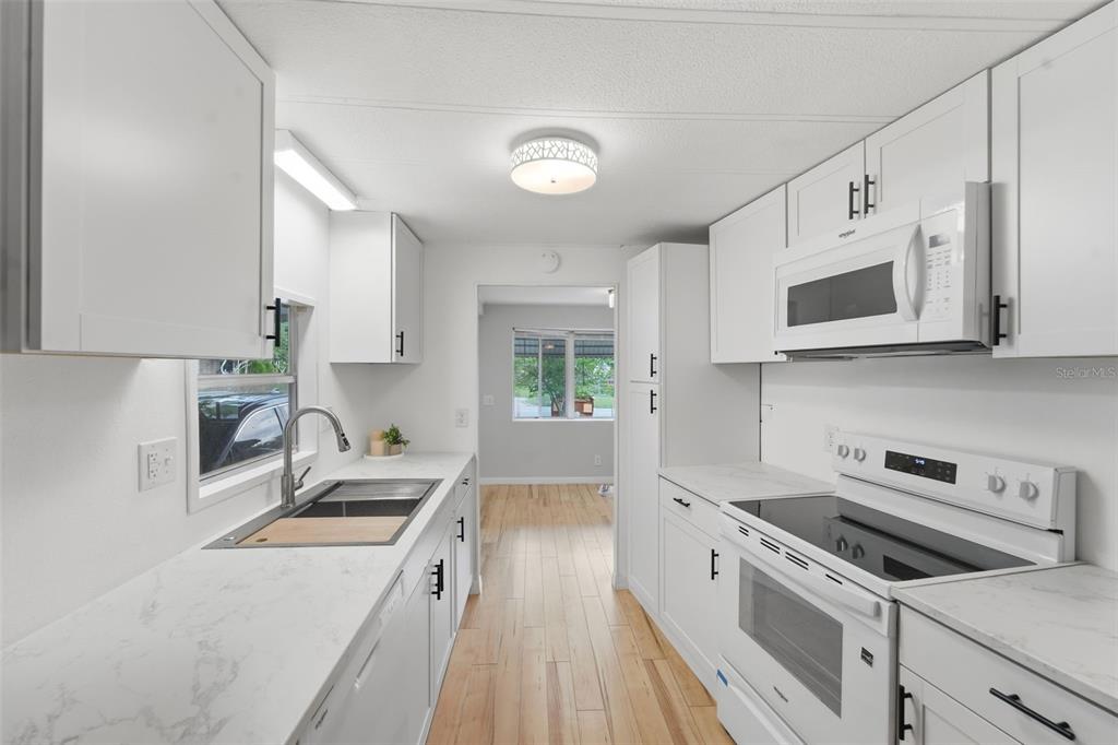 A galley kitchen features white cabinets, light countertops, stainless steel appliances, and wood-look flooring — 4128 WOODLAND CIRCLE, DELAND, FL