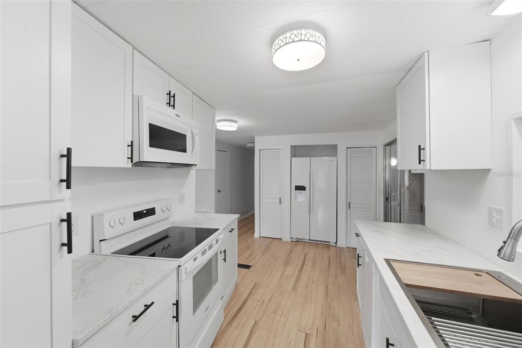 A bright kitchen features white cabinets, stainless steel appliances, and light wood flooring — 4128 WOODLAND CIRCLE, DELAND, FL