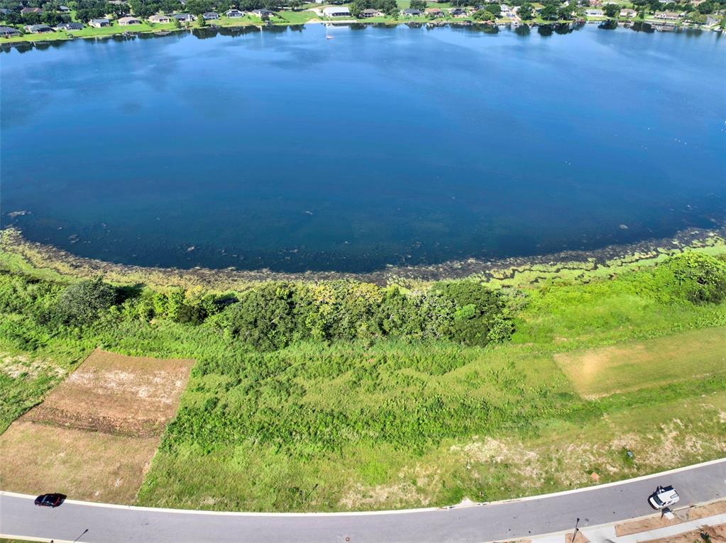 An aerial view shows a vacant grassy lot bordering a large lake and a paved road — 4283 JULIANA LAKE DRIVE, AUBURNDALE, FL