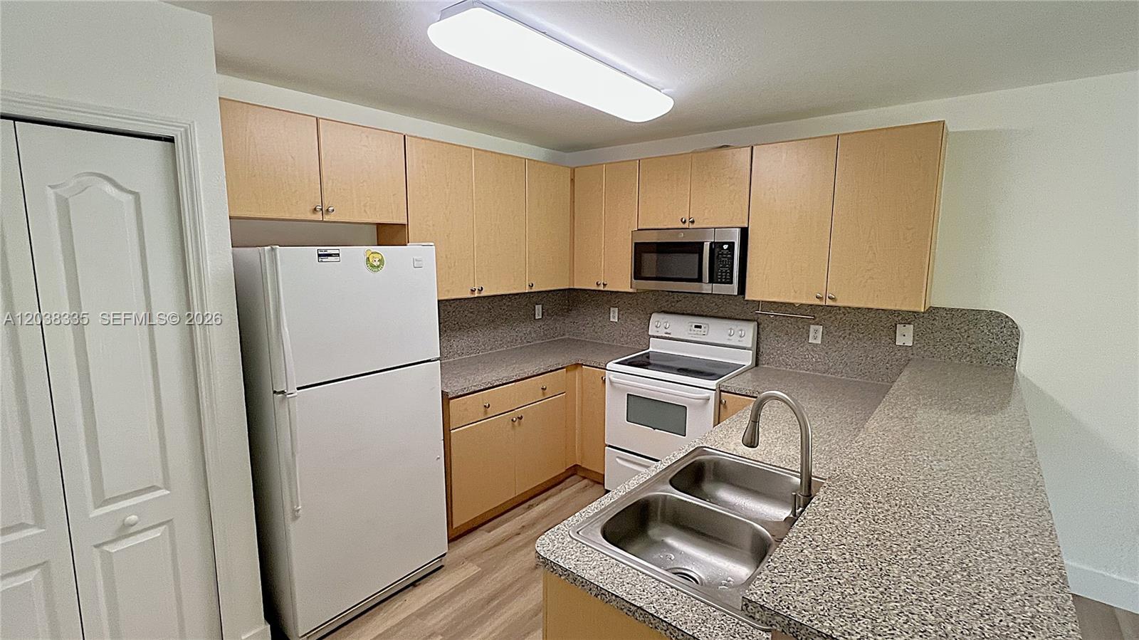 A kitchen features light wood cabinets, speckled countertops, white appliances, and a double-basin sink — 22721 SW 88th Pl # 19, Cutler Bay FL 33190, CUTLER BAY, FL