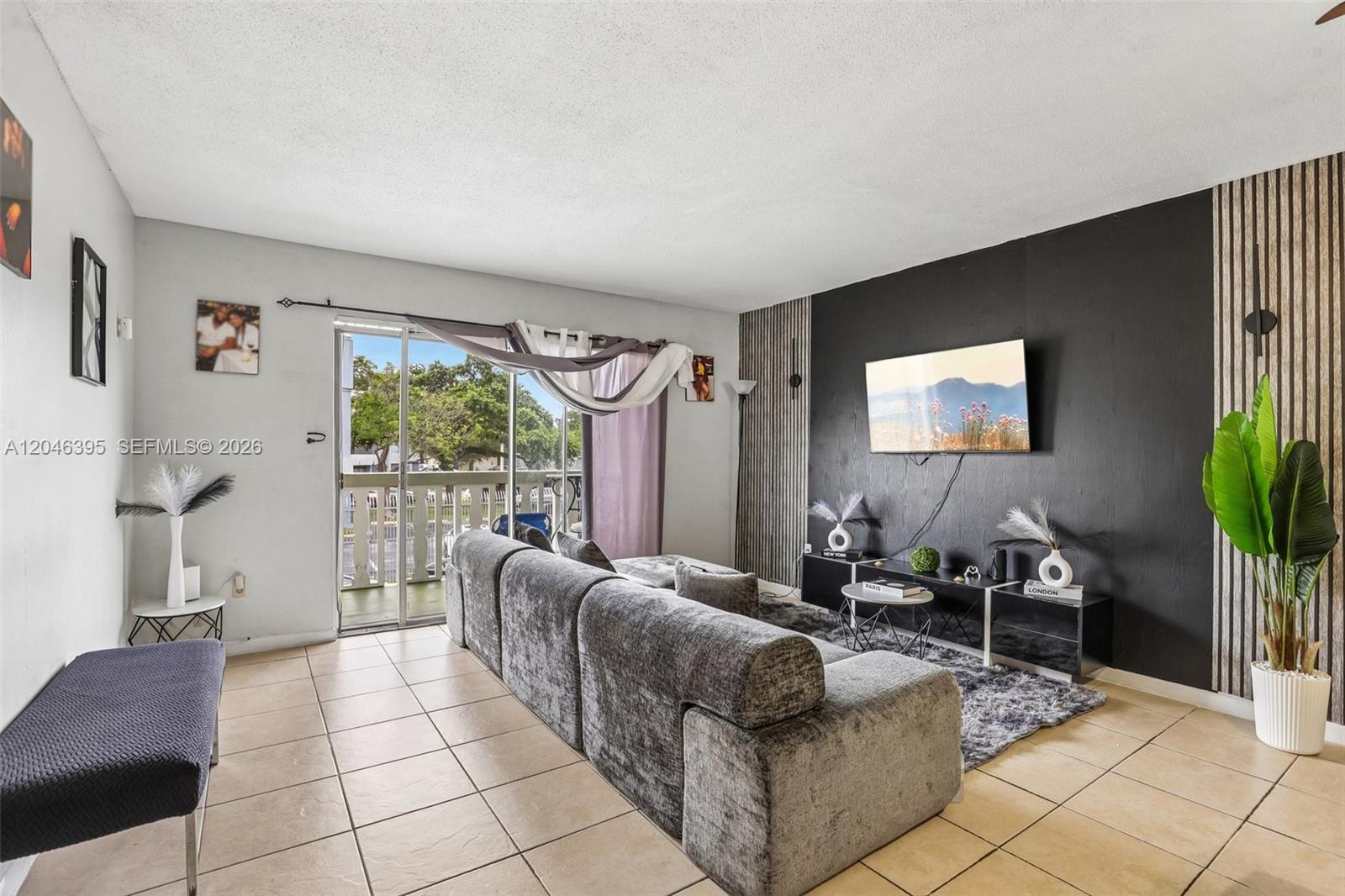 A living room features a grey sectional sofa, a black accent wall with a television, and tile flooring — 15225 NE 6th Ave # B208, Miami FL 33162, MIAMI, FL