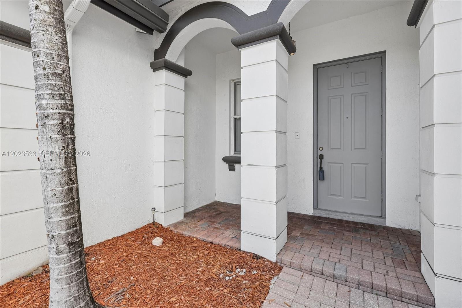 A covered entryway features a gray door, brick pavers, and white columns with arched trim — 7616 NW 114th Path # 7616, Doral FL 33178, DORAL, FL