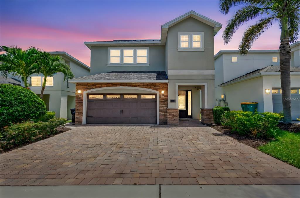 A two-story house with a stone-accented garage and a paved driveway at sunset — 311 PENDANT COURT, KISSIMMEE, FL