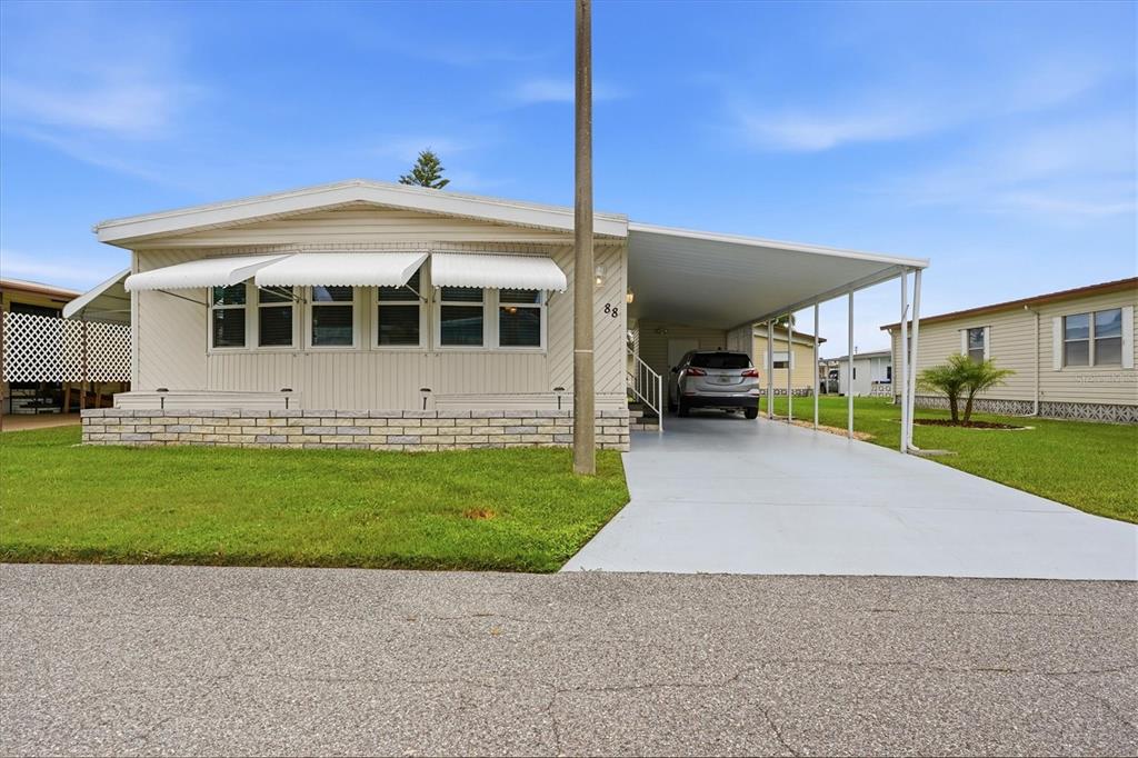 A single-story manufactured home with a carport, light siding, and a stone-style base — 808 53RD AVENUE E UNIT 88, BRADENTON, FL