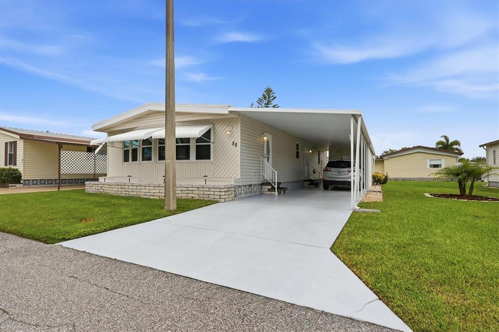 A single-story manufactured home with a carport, concrete driveway, and light-colored siding — 808 53RD AVENUE E UNIT 88, BRADENTON, FL