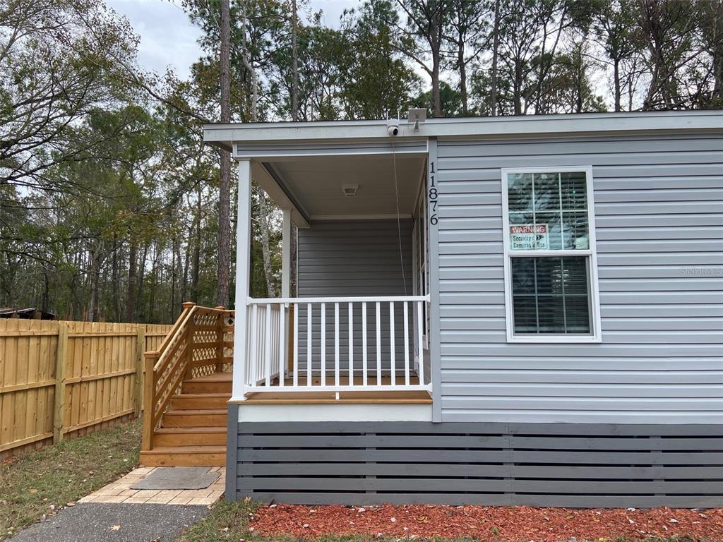 A light gray manufactured home features a covered front porch with white railings and stairs — 11876 KEYLIME DRIVE, NEW PORT RICHEY, FL