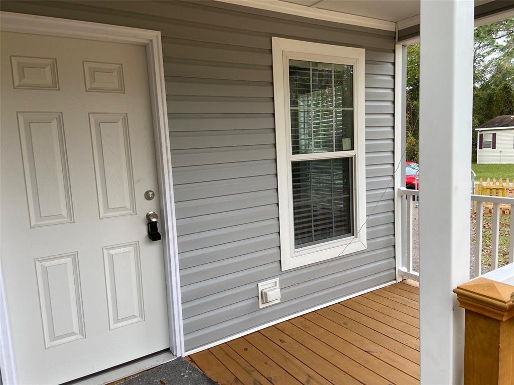 A white front door and a window are set into gray siding on a wooden porch — 11876 KEYLIME DRIVE, NEW PORT RICHEY, FL