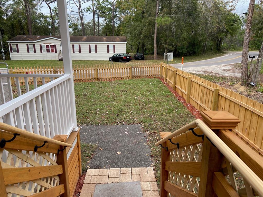 A view from a wooden porch staircase looking out over a fenced-in grassy yard — 11876 KEYLIME DRIVE, NEW PORT RICHEY, FL