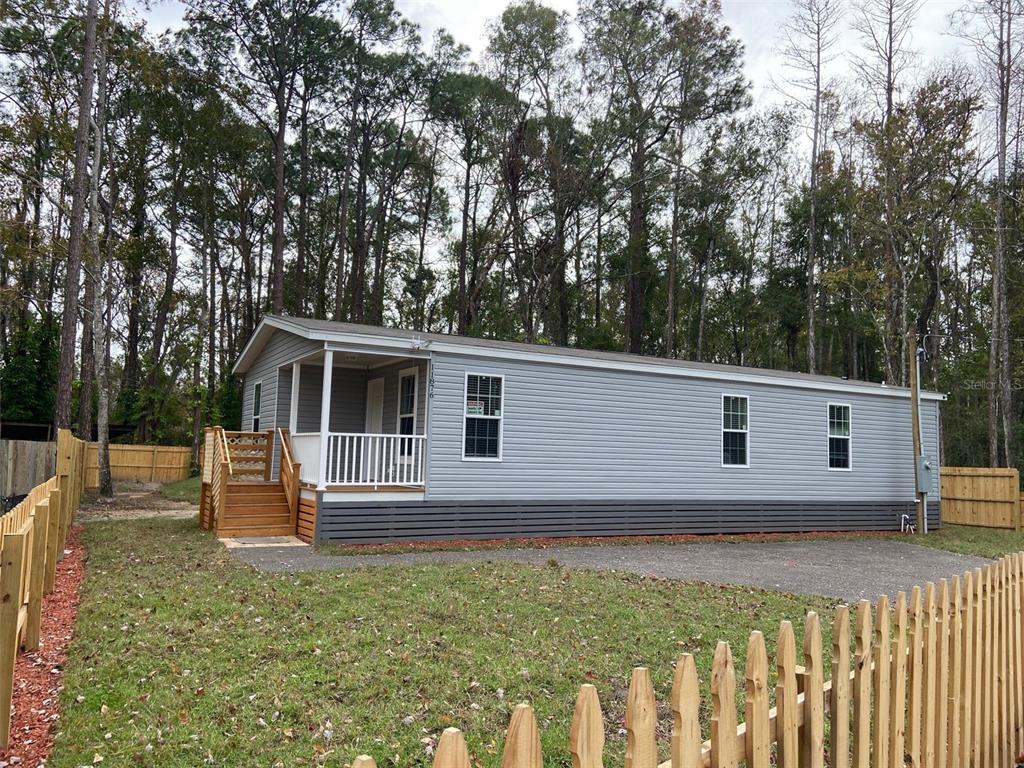 A light gray manufactured home with a front porch sits on a lot with fencing — 11876 KEYLIME DRIVE, NEW PORT RICHEY, FL