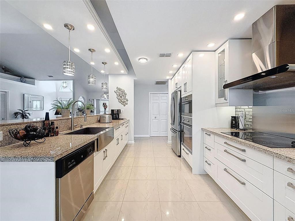 A modern kitchen features white cabinetry, granite countertops, stainless steel appliances, and tile flooring — 13627 GLAZE BROOK DRIVE, HUDSON, FL