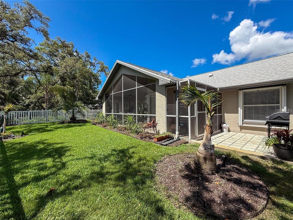 A backyard view featuring a screened-in porch, a small palm tree, and a white fence — 13627 GLAZE BROOK DRIVE, HUDSON, FL