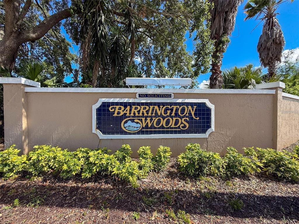 A tan stucco wall displays a blue tiled sign for Barrington Woods under leafy trees — 13627 GLAZE BROOK DRIVE, HUDSON, FL
