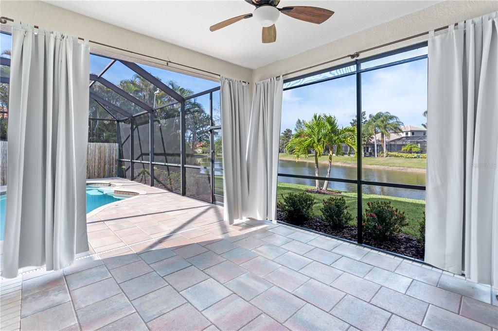 A tiled, screened-in patio overlooks a swimming pool and a lake with palm trees — 14717 BOWFIN TERRACE, BRADENTON, FL