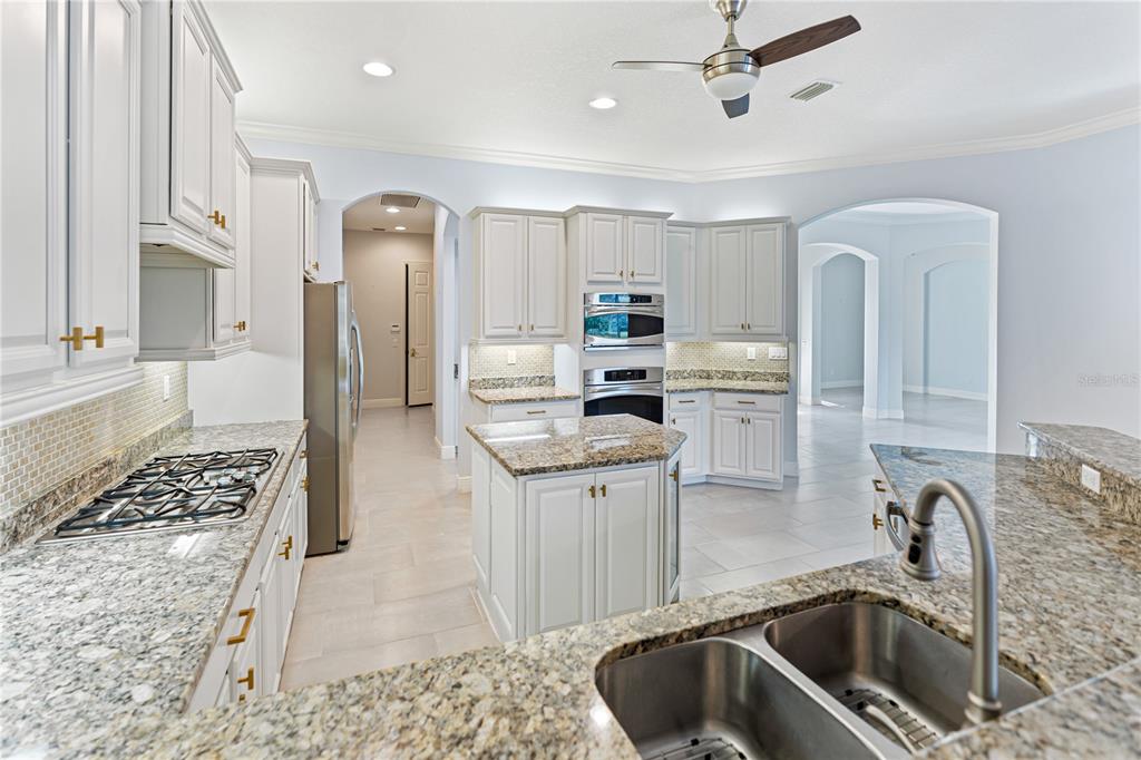 A kitchen features white cabinets, granite countertops, a central island, and stainless steel appliances — 14717 BOWFIN TERRACE, BRADENTON, FL