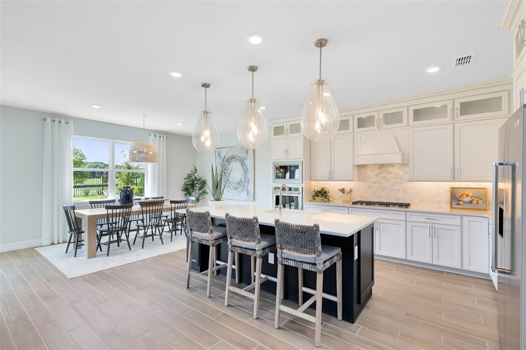 A modern kitchen features a dark island with bar stools, white cabinetry, and an adjacent dining area — 4746 HARRINGTON FIELDS DRIVE, DAVENPORT, FL