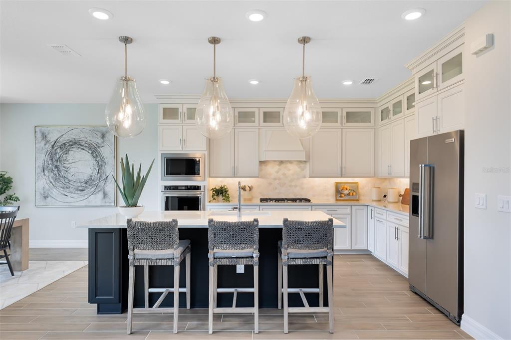 A modern kitchen features a dark island with three stools, white cabinetry, and stainless appliances — 4746 HARRINGTON FIELDS DRIVE, DAVENPORT, FL