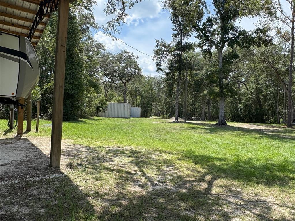 A grassy yard with trees, a covered RV parking area, and two storage containers — 1551 NE 930TH STREET, OLD TOWN, FL