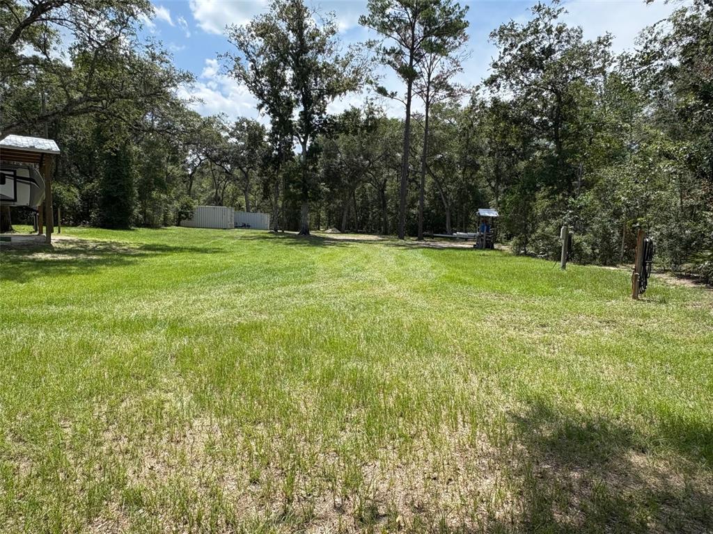 A grassy, wooded lot features a covered RV pad and a small storage structure — 1551 NE 930TH STREET, OLD TOWN, FL