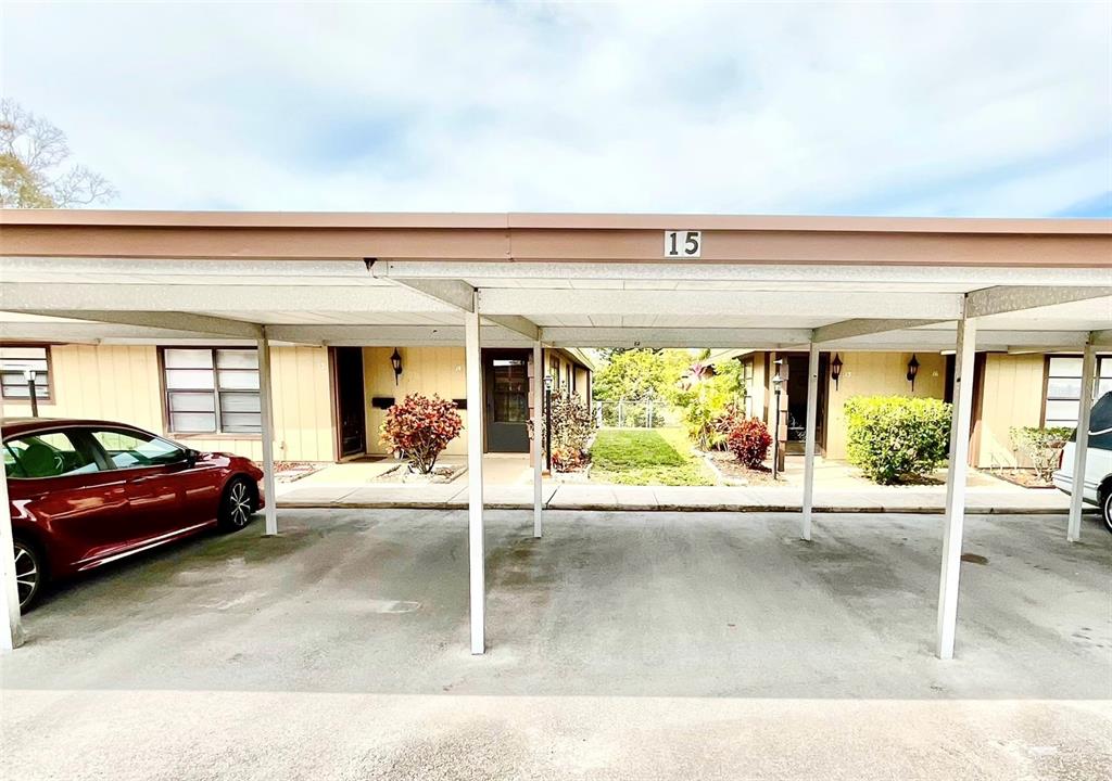 A covered carport area sits in front of two residential units with tan siding — 1980 TAHITIAN PLACE UNIT 15, DUNEDIN, FL