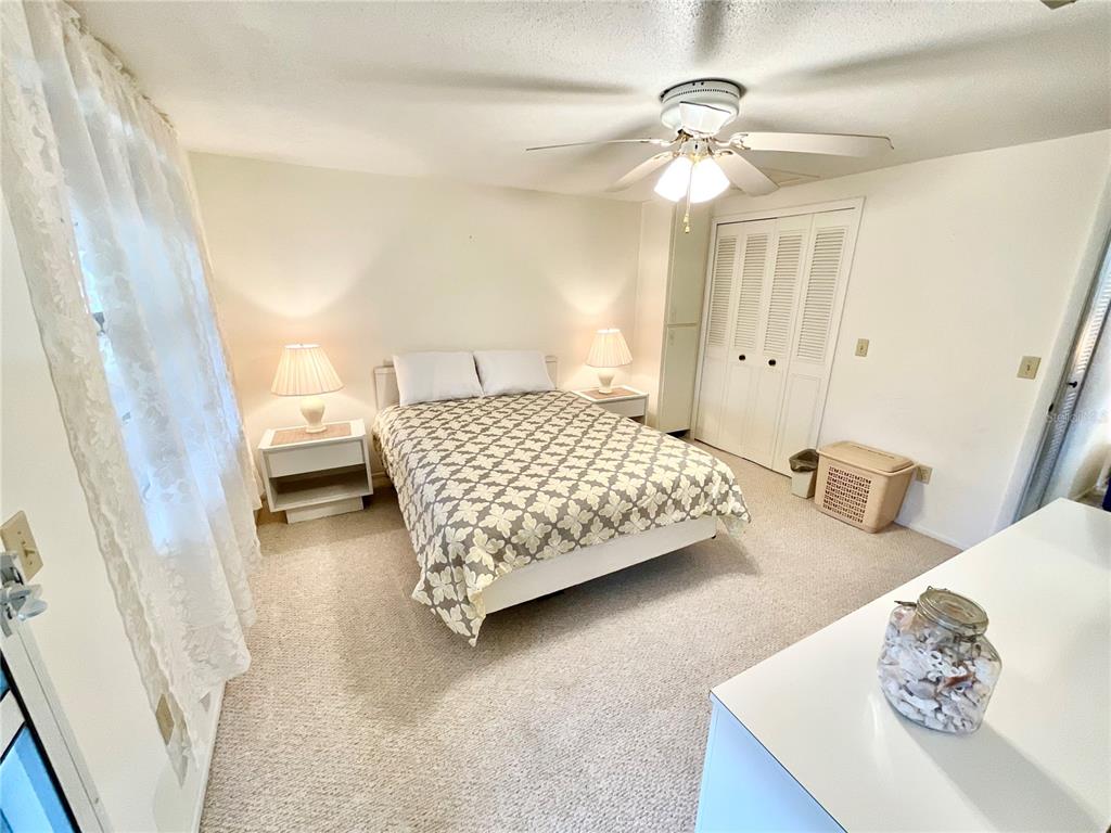 A bedroom features a bed with a patterned quilt, two nightstands, and a ceiling fan — 1980 TAHITIAN PLACE UNIT 15, DUNEDIN, FL