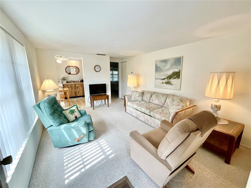 A living room features a sofa, two armchairs, a television, and light-colored carpeting — 1980 TAHITIAN PLACE UNIT 15, DUNEDIN, FL
