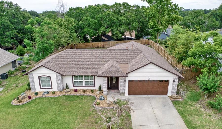 An aerial view of a single-story house with a brown roof, garage, and landscaped yard — 831 FORESTWOOD DR, MINNEOLA, FL