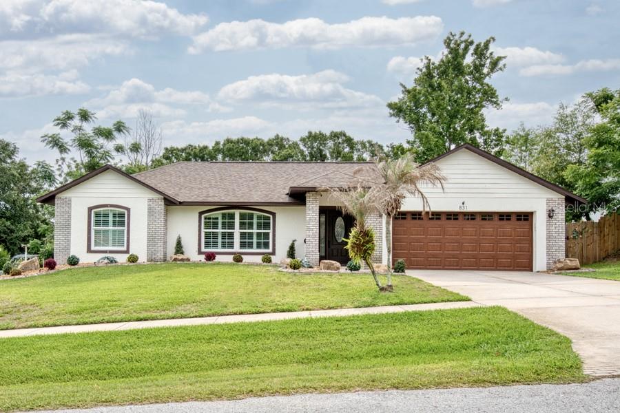 A single-story house with white stucco walls, brick accents, and a brown garage door — 831 FORESTWOOD DR, MINNEOLA, FL