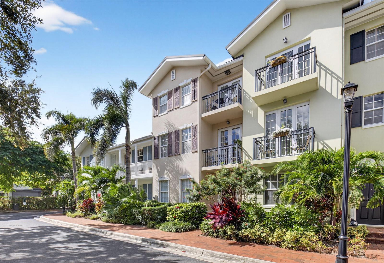 A three-story apartment building with balconies, shutters, and tropical landscaping along a brick sidewalk — 1054 E Heritage Club Circle, Delray Beach FL 33483, DELRAY BEACH, FL