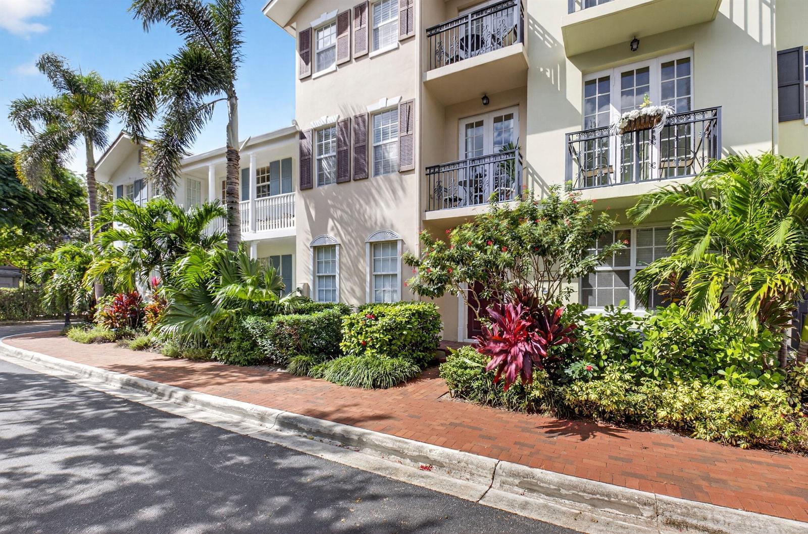A multi-story building with balconies, shutters, and lush landscaping along a brick sidewalk — 1054 E Heritage Club Circle, Delray Beach FL 33483, DELRAY BEACH, FL