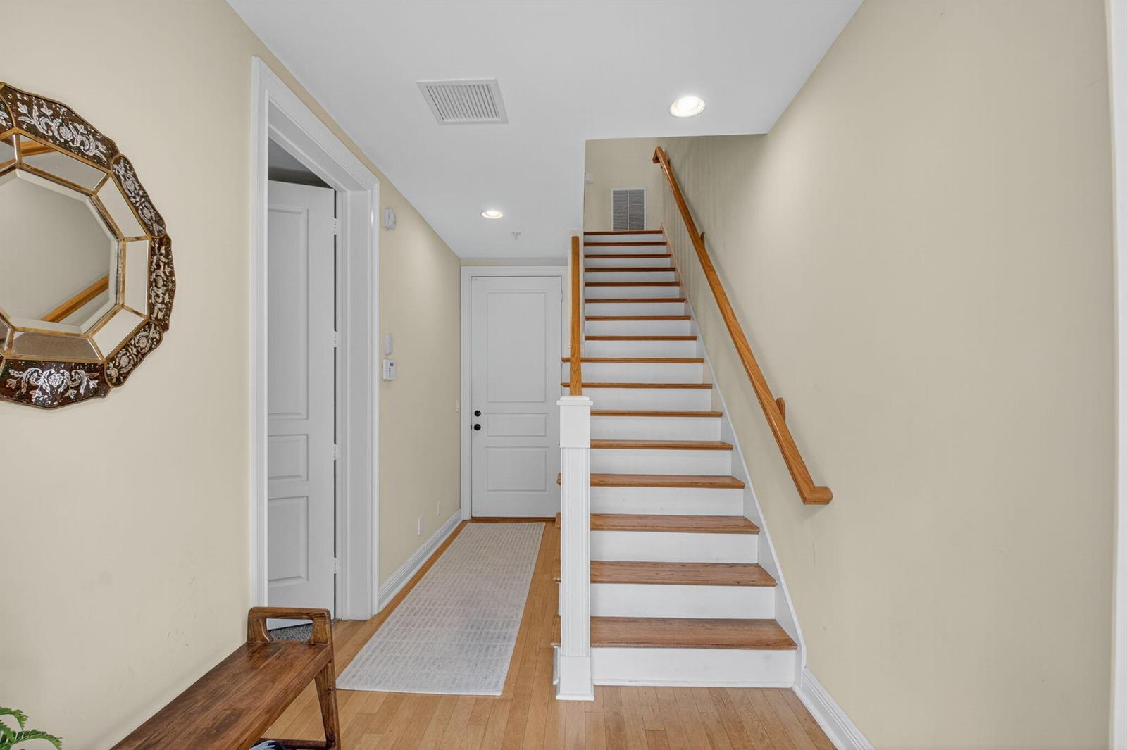 An interior entryway features a wooden staircase, a white door, and a decorative wall mirror — 1054 E Heritage Club Circle, Delray Beach FL 33483, DELRAY BEACH, FL