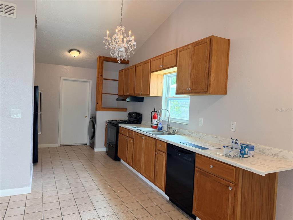 A kitchen features light wood cabinets, a white countertop, a black dishwasher, and a chandelier — 208 FLAMINGO DRIVE, APOLLO BEACH, FL