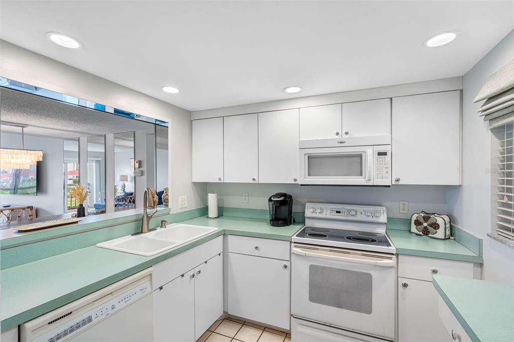 A kitchen features white cabinets, light green countertops, a white appliance suite, and a pass-through window — 7871 SAILBOAT KEY BOULEVARD S UNIT 106, SOUTH PASADENA, FL