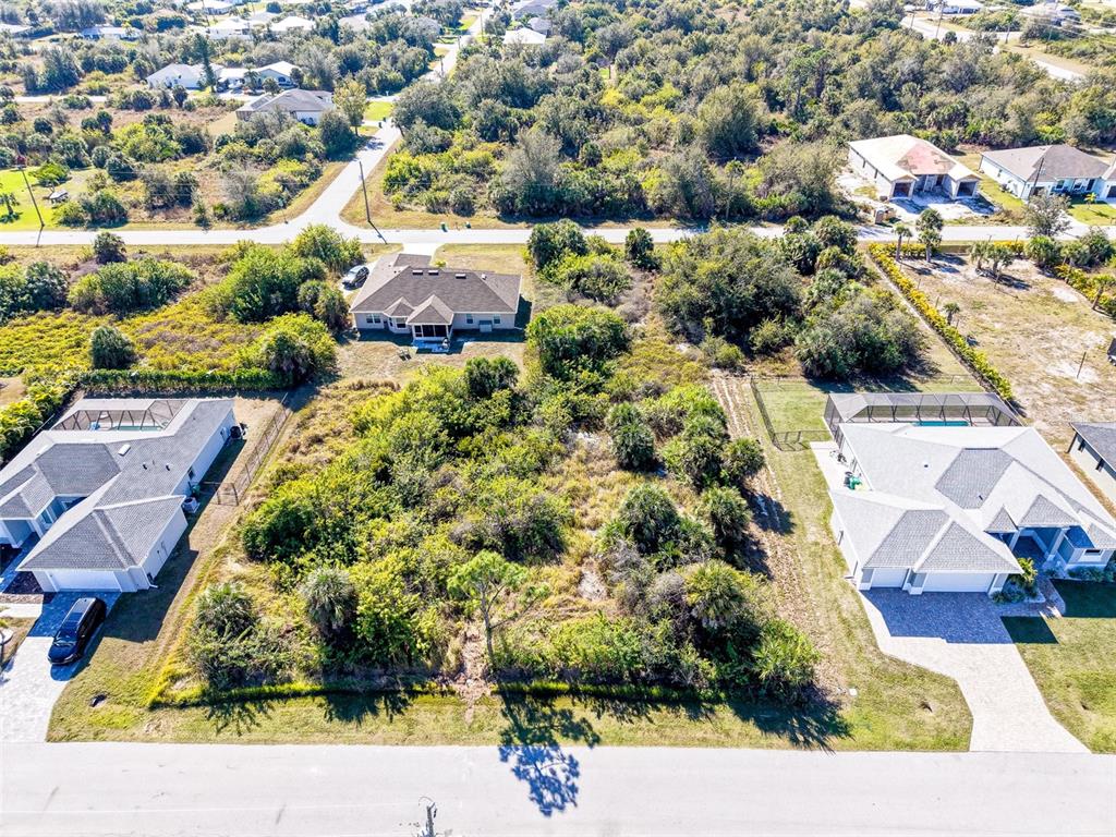 An aerial view shows a vacant, wooded lot situated between two residential houses — 9309 PANAMA CIRCLE, PORT CHARLOTTE, FL