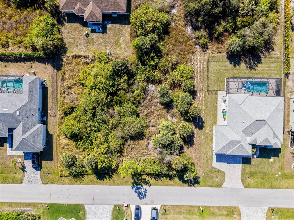 An aerial view shows a vacant, wooded residential lot situated between two houses with pools — 9309 PANAMA CIRCLE, PORT CHARLOTTE, FL