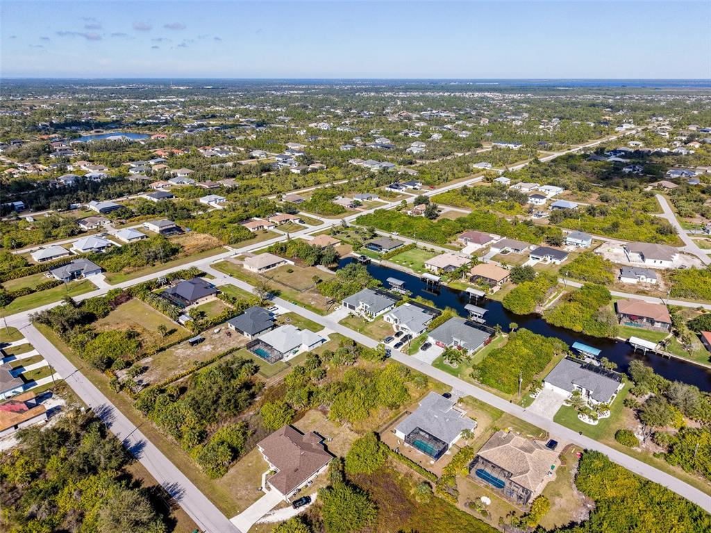 An aerial view shows suburban houses and a canal surrounded by dense green vegetation — 9309 PANAMA CIRCLE, PORT CHARLOTTE, FL