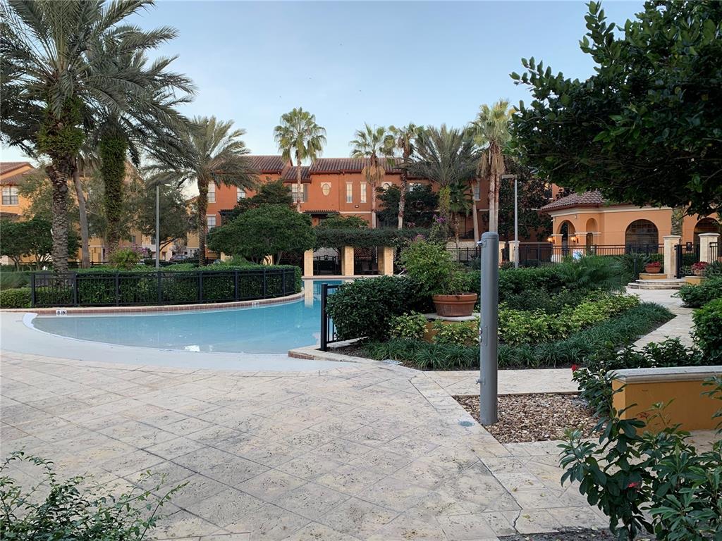 A swimming pool sits in front of a multi-story building with palm trees and landscaping — 5572 METROWEST BOULEVARD UNIT 5-209, ORLANDO, FL