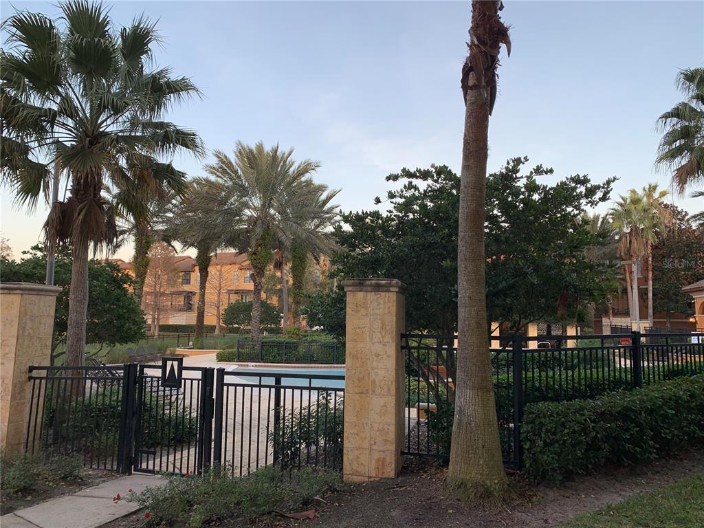 A black metal fence surrounds a swimming pool area with palm trees and apartment buildings — 5572 METROWEST BOULEVARD UNIT 5-209, ORLANDO, FL