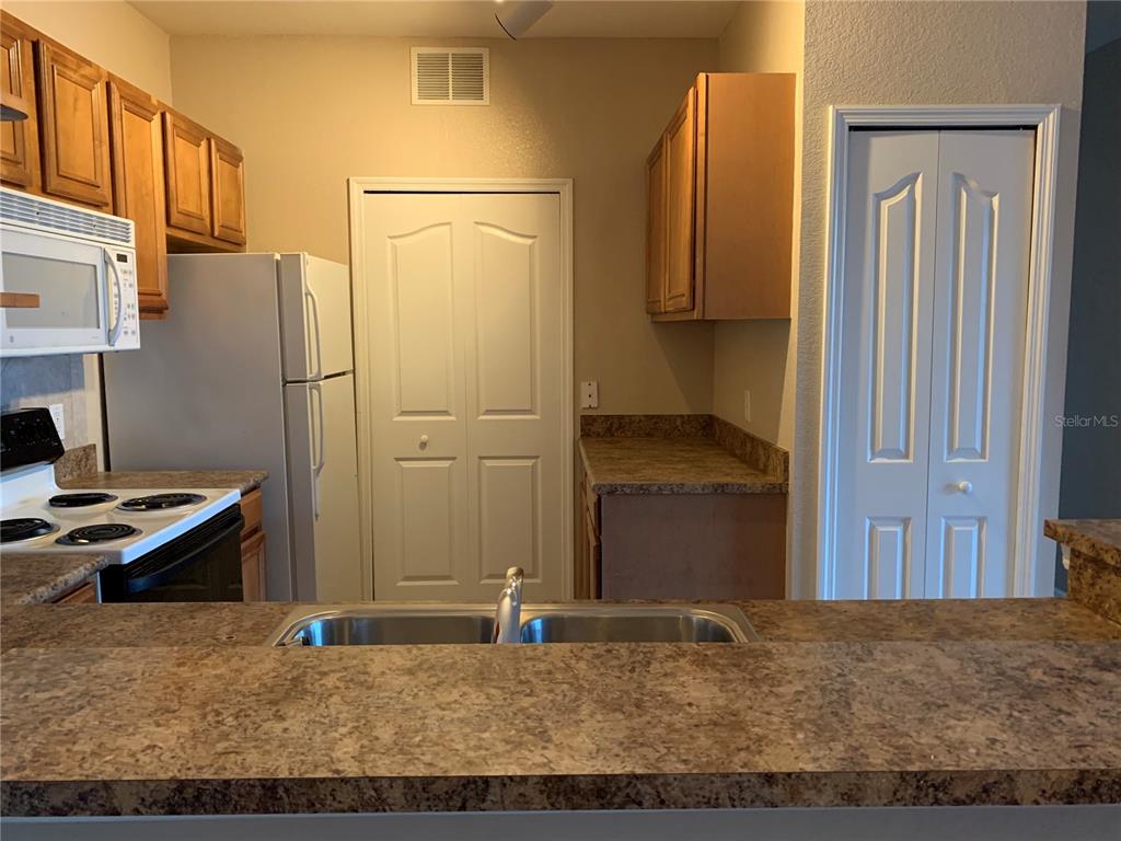A kitchen features wood cabinets, laminate countertops, a white refrigerator, and a double-basin sink — 5572 METROWEST BOULEVARD UNIT 5-209, ORLANDO, FL
